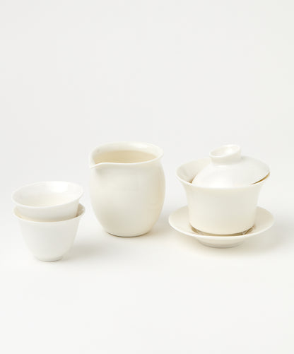A white porcelain gaiwan with a tilted lid, a pitcher, and two stacked teacups.