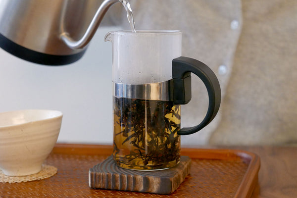 Pouring hot water into a French press with tea leaves.