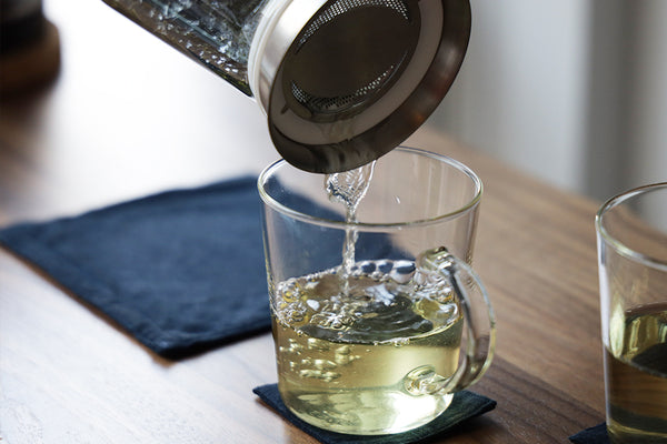 Pouring brewed tea into a glass cup from a tea brewing pitcher.