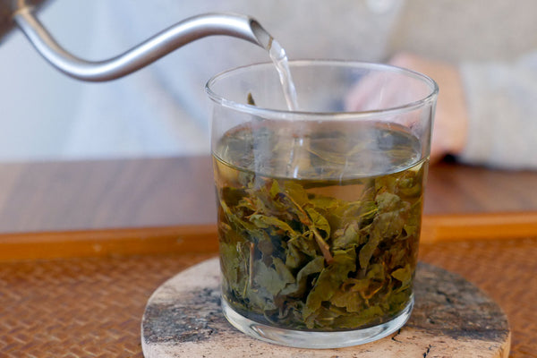 Pouring hot water over tea leaves in a glass cup.