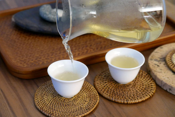 Pouring tea from a glass pitcher into two small cups