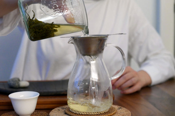 Pourin tea into a glass pitcher with a metal strainer.