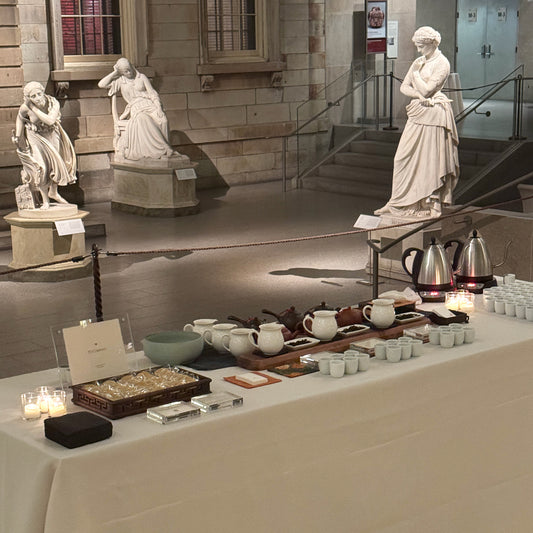 A tea tasting setup with teapots, cups, tea leaves, and snacks in a museum setting.