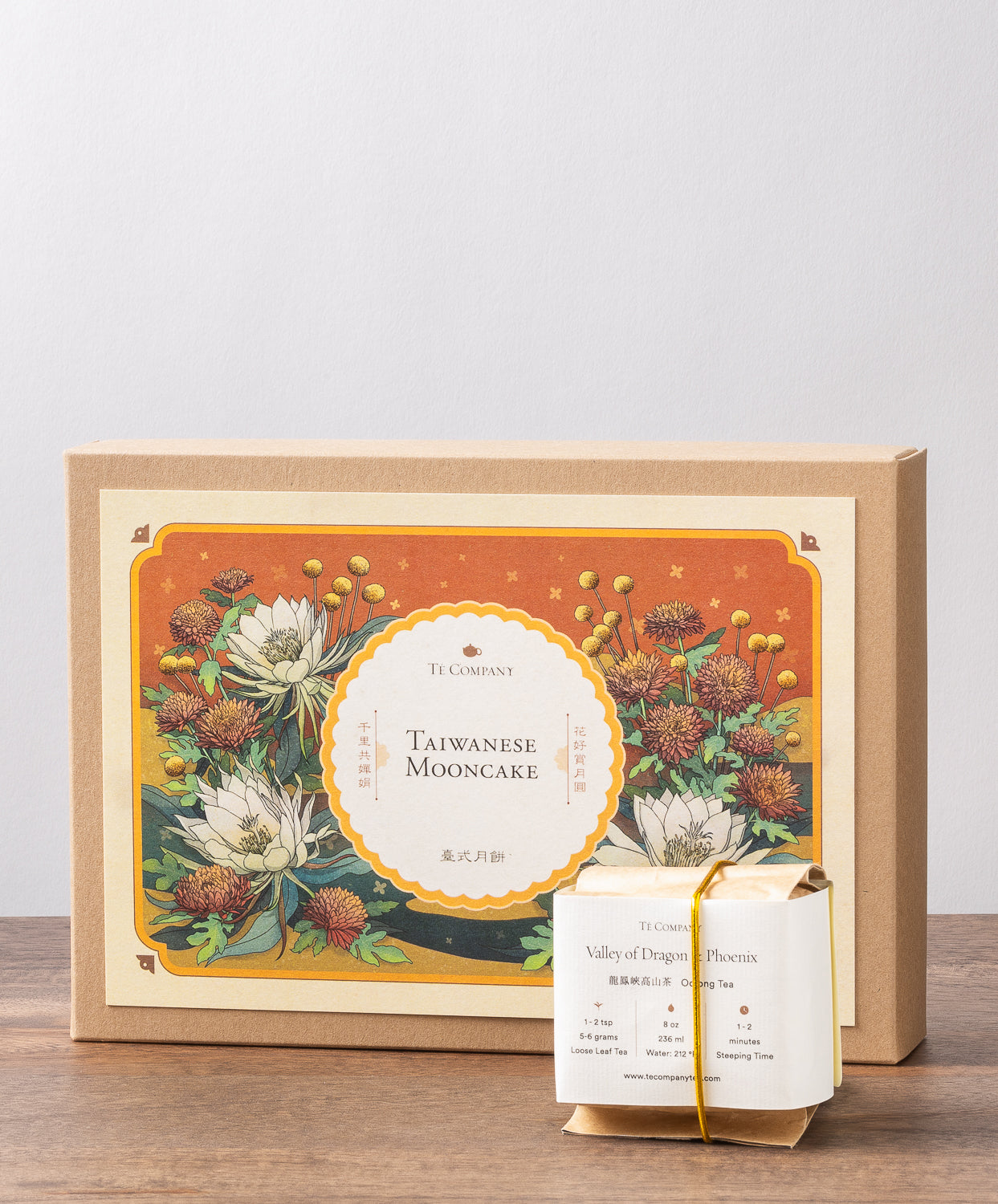 A box labeled Taiwanese Mooncake by Te Company with an floral illustration featuring flowers, along with a wrapped package of oolong tea.