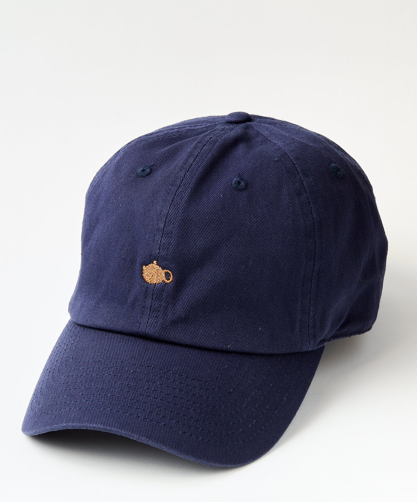 Navy blue baseball cap with a small embroidered golden teapot design on the front.