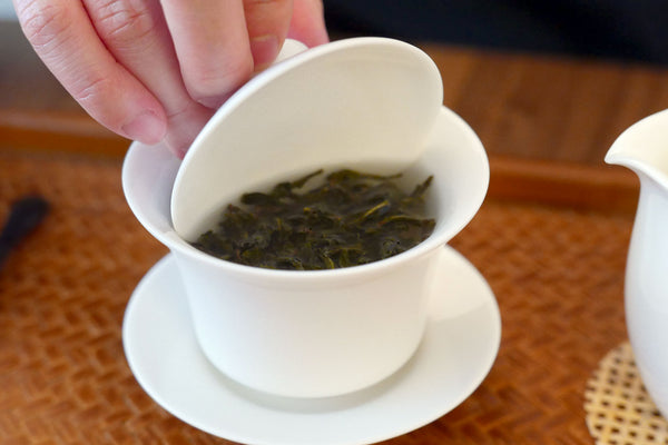 Hand using a gaiwan lid to stir steeping tea leaves.