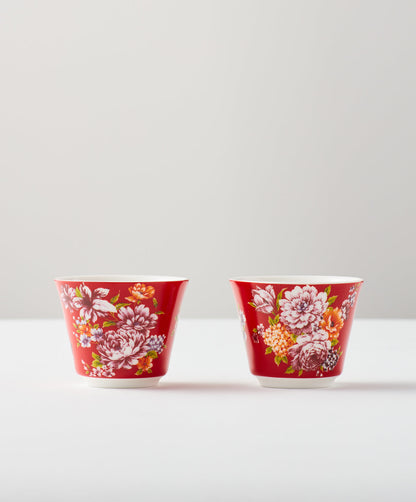 Set of two red floral ceramic cups on a white surface.