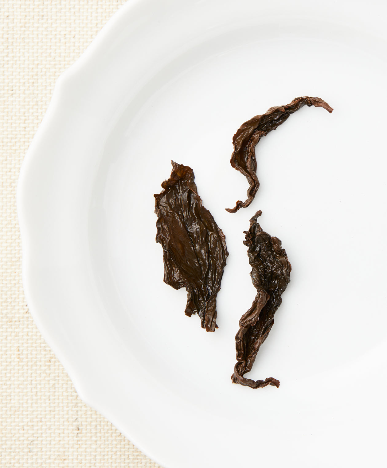 A set of steeped tea leaves with a dark brown color and various shapes displayed on a white plate.