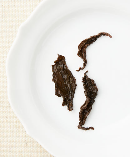 A set of steeped tea leaves with a dark brown color and various shapes displayed on a white plate.