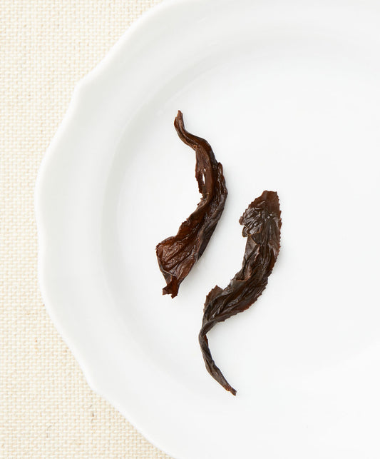 Two steeped tea leaves with a dark brown color displayed on a white plate.