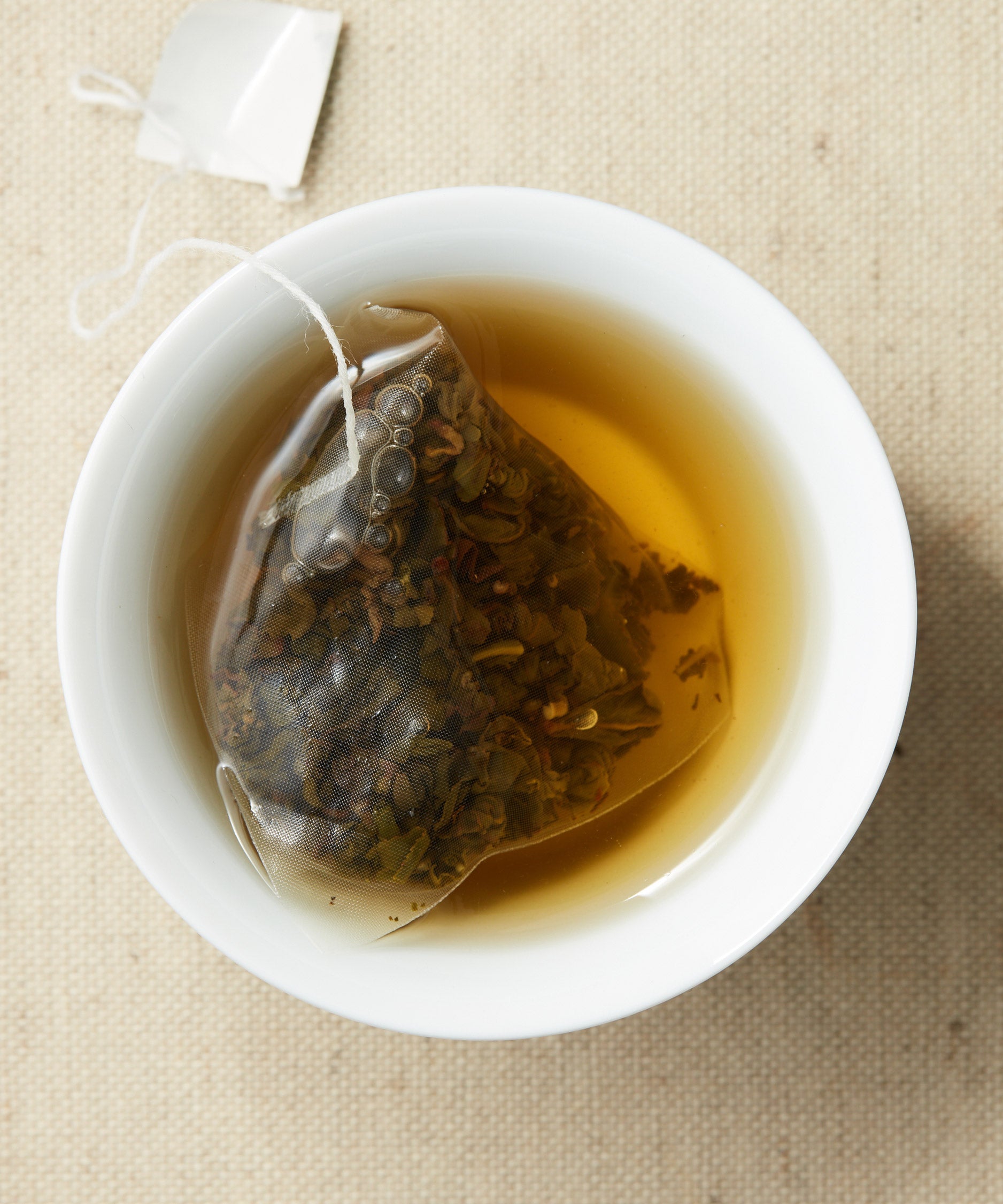 A cup of steeped tea with a pyramid-shaped tea sachet containing loose leaves, submerged in the liquid.