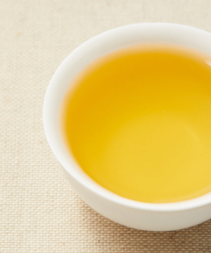 A close-up of a white teacup filled with golden-yellow tea on a beige textured background.
