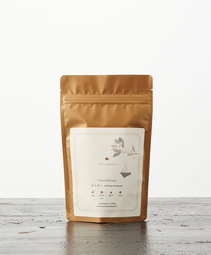 A gold resealable pouch labeled Oriental Beauty by Te Company, featuring elegant botanical artwork, set on a wooden surface.
