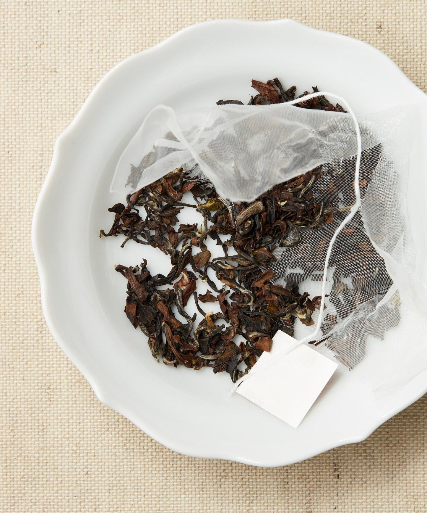 A pyramid-shaped tea sachet with loose leaves scattered around it on a white plate.