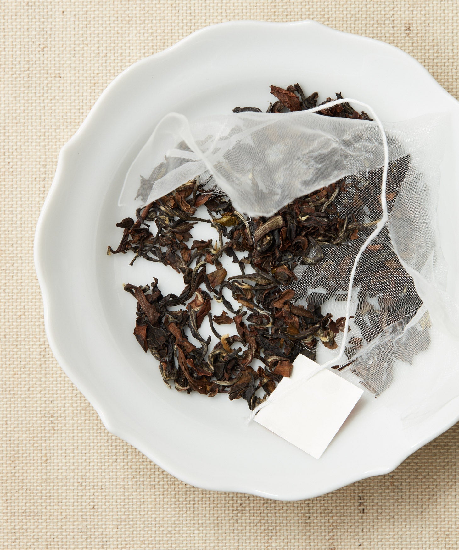 A pyramid-shaped tea sachet with loose leaves scattered around it on a white plate.