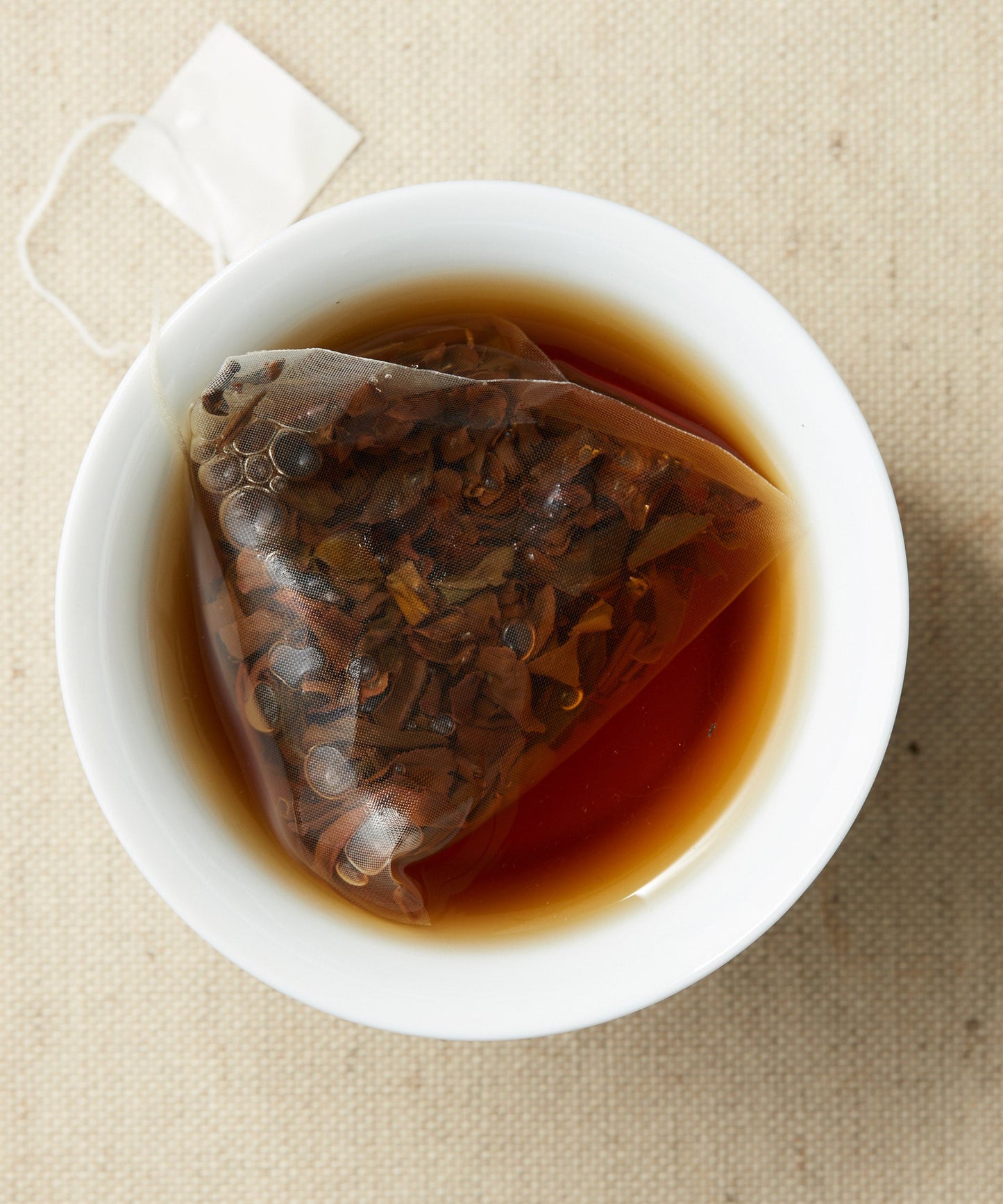 A cup of steeped tea with a pyramid-shaped tea sachet containing loose leaves, submerged in the liquid.
