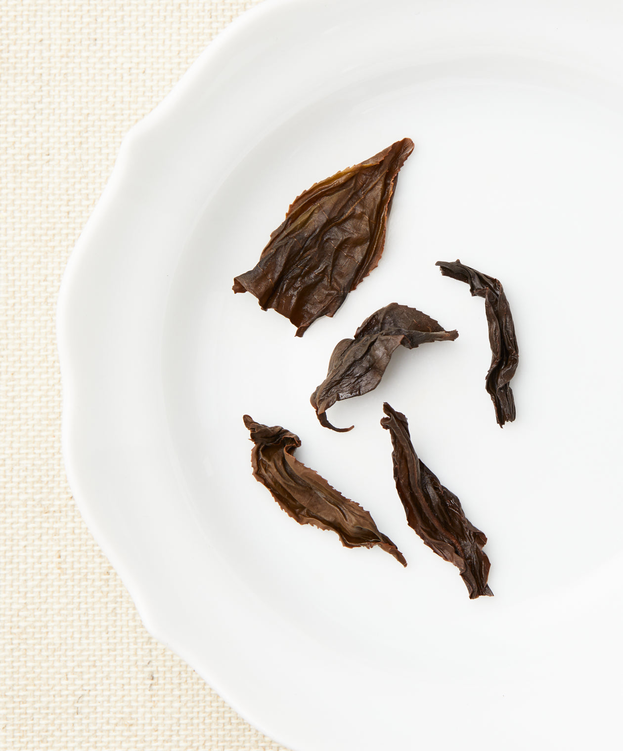 A set of steeped tea leaves with a dark brown color and various shapes displayed on a white plate.