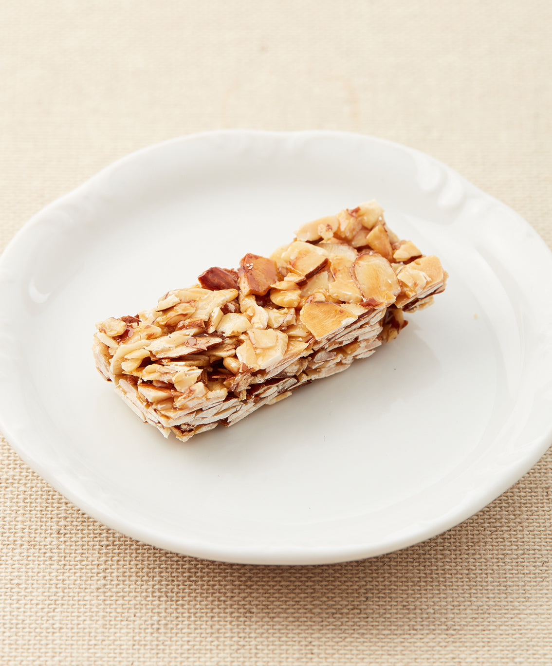 A side view of an almond bar on a white plate, highlighting its layered and nutty texture.