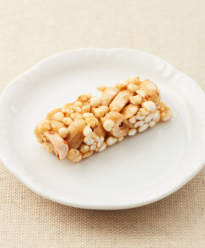 A side view of a peanut and millet bar on a white plate, showing its airy texture and caramelized appearance.