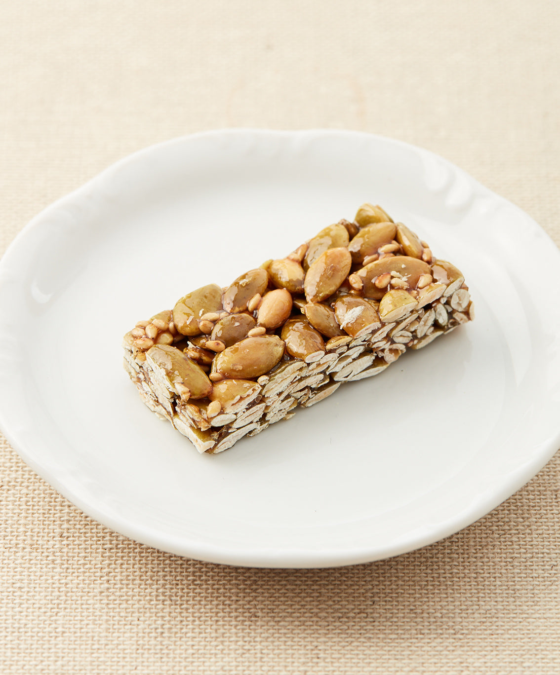 A side view of a pumpkin seed bar on a white plate, showing the layered texture of seeds and syrup.