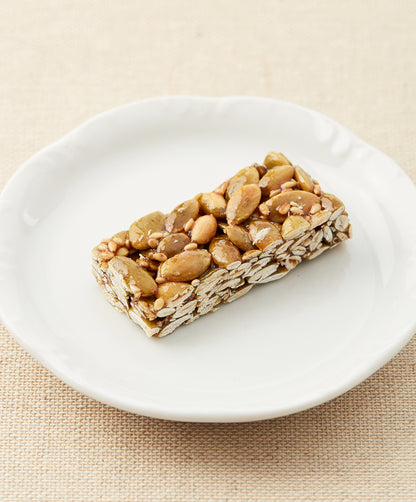 A side view of a pumpkin seed bar on a white plate, showing the layered texture of seeds and syrup.