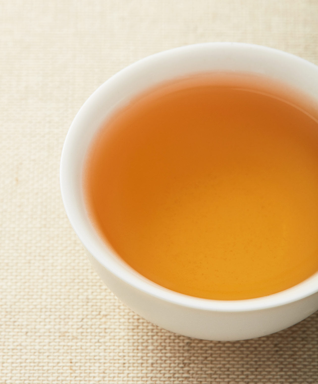 A cup of golden White Peony tea on a textured surface.